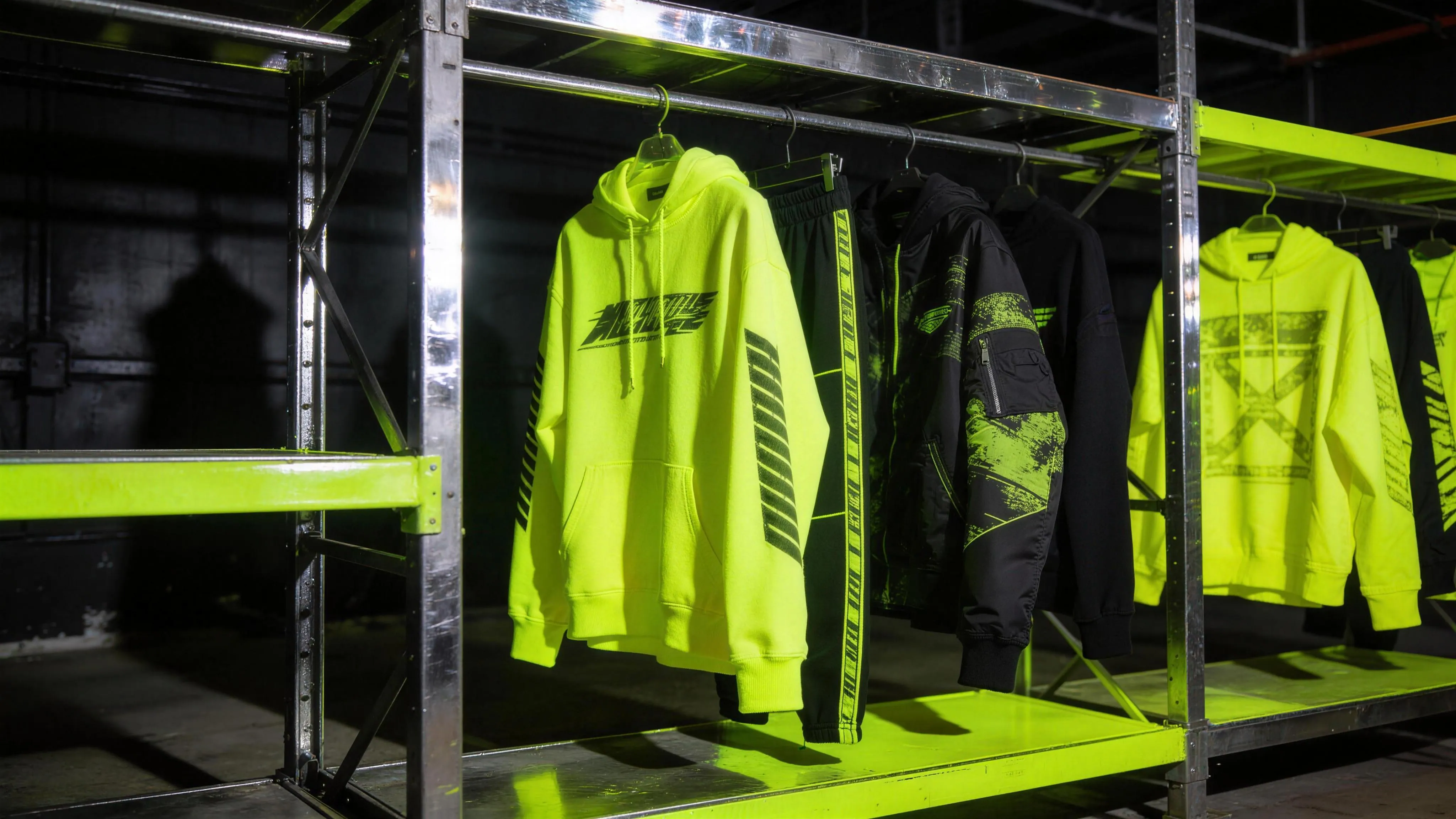 Acid-yellow streetwear hanging on a chrome rack in a dark studio